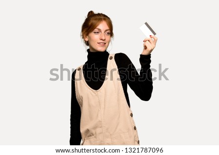Young redhead woman holding a credit card and thinking over grey background