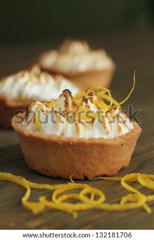 Three lemon tarts with meringue and fresh mint leave on wooden table