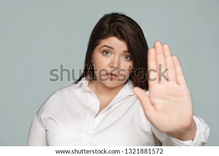 Stay away from me. Serious displeased young brunette chubby female secretary in formal wear staring at camera, outstretching hand, making stop gesture with palm, expressing refusal or rejection