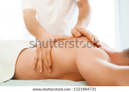 Image from side of male therapist massaging man back.
