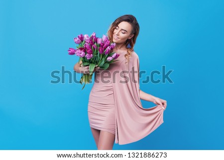 Young happy smiling redhead woman holding bouquet of colorful spring flowers isolated on blue background. Pink tulips, festive bouquet in honor of women's day on March 8 or birthday