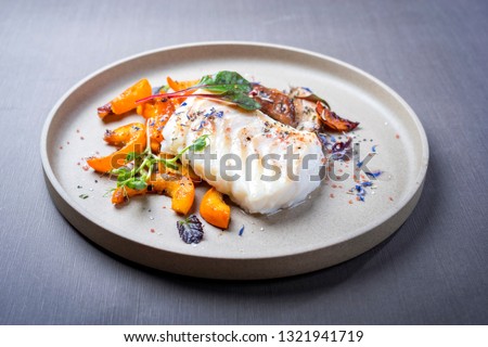 Fried Danish skrei cod fish filet with pumpkin, mushroom and lettuce as closeup on a modern design plate 