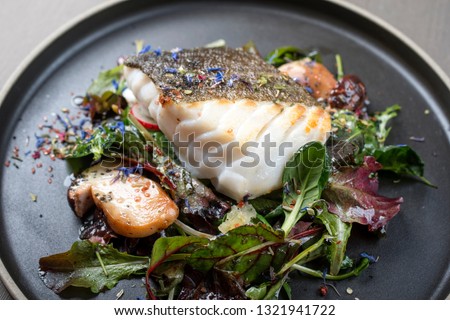 Fried Danish skrei cod fish filet with porcini mushroom and lettuce as closeup on a modern design plate 