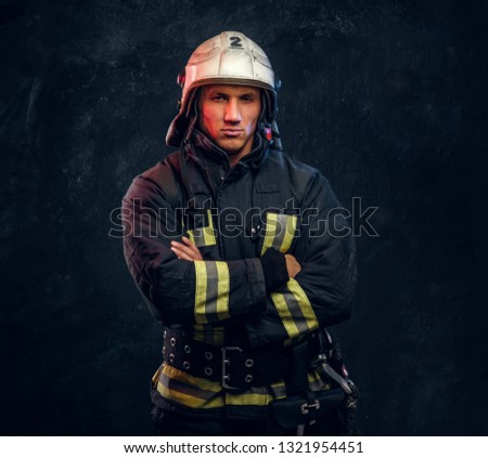 Manly firefighter in helmet looks into camera in studio on black background