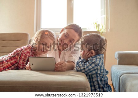 Happy mother with children watching cartoons on tablet and having fun while spending time together at home