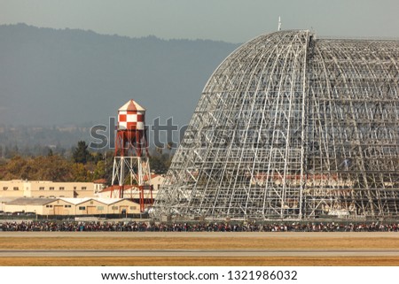 View of an airplane hangar under construction and a crowd at an airshow