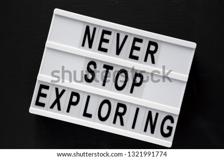 Lightbox with text 'Never stop exploring' over black background, top view. Overhead, flat lay, from above. Close-up.