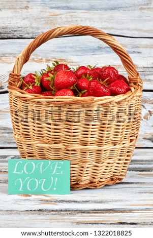 Basket of strawberries and text love you. Wicker basket filled with fresh fragrant strawberries on wooden background. Love confession with fruits.