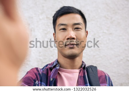 Portrait of a confident young Asian man standing on a sidewalk in the city taking a selfie