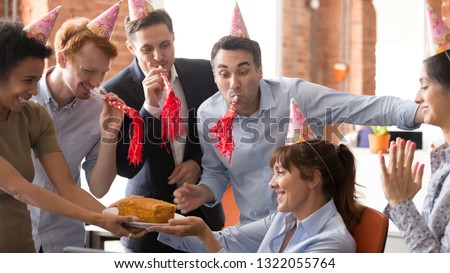 Office employees people in party hats congratulate happy female colleague make surprise, friendly diverse corporate team blow whistles presenting cake to woman boss celebrating birthday having fun