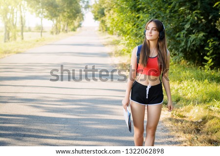 Young beautiful girl walks down the road with a map in the countryside listening to music and admiring the beauty of nature