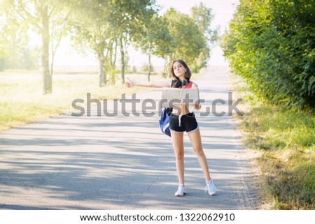 Tired tourist girl tries to hitchhike a car at the country road. Exhausted tourist with heavy bag stops a car to bring herself to the town