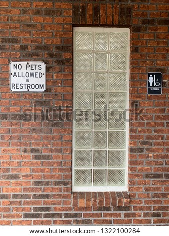 No Pets Allowed in Restroom sign on brick wall with glass cube window at women's restroom