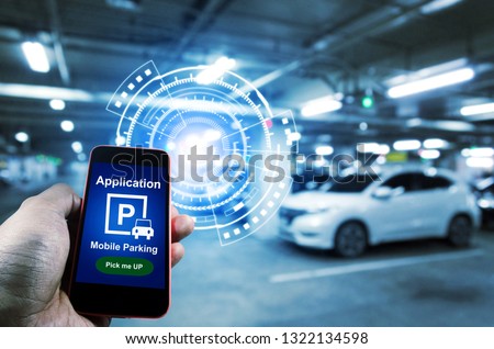 Pick me up, mobile smart phone in hand using application for intelligent car park with digital hologram on blurred parking car background, mobile auto parking, network and online technology concept