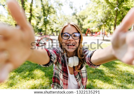 Blithesome caucasian girl in headphones making selfie on nature background. Carefree european woman enjoying sunny day.