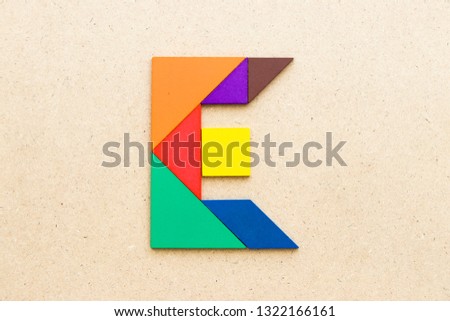 Tangram puzzle in alphabet letter E shape on wood background