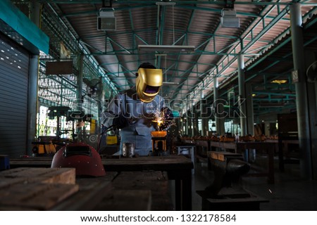 Welders are working to weld metal that has light from welding, splashing out into the workplace, which is an industrial factory with protective sets and masks.