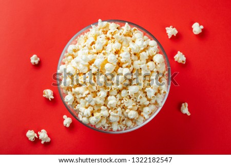 Glass bowl of salty popcorn on a red background. Top view with copy space. Flat lay