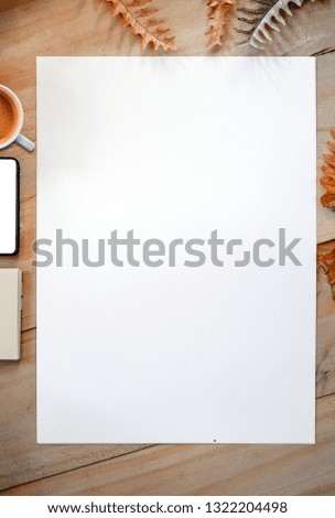 Top view of pure white page with cup of coffee, smartphone and notebook on wooden table and dried leaves background. Design concept.