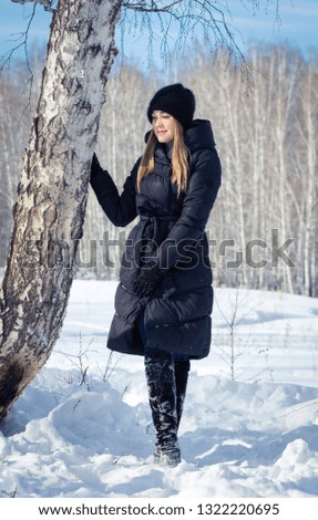 A young blonde girl is walking in the woods in winter. Girl model posing among trees and snow.