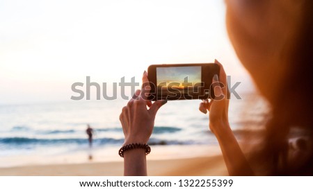Woman taking photos with her smartphone on beach during sunset or sunrise 

