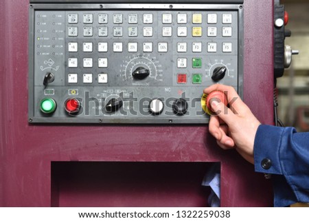 Worker in blue workwear holds hands on the control panel of the CNC machine. Close-up
