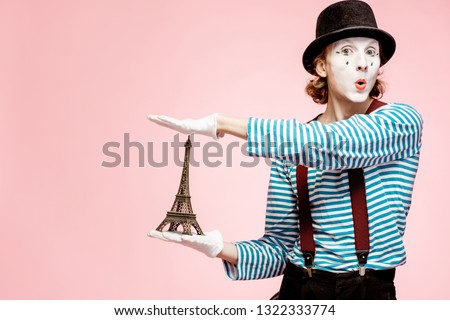 Pantomime with white facial makeup posing with Eiffel tower on the pink background. French mime concept