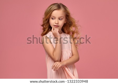 Little girl with a blond curly hair, in a pink dress is posing for the camera