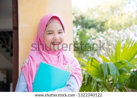 Pretty muslim girl holding book and smiles at school.