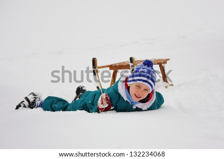 Boy lying in the snow in front of his sleigh