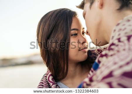 Affectionate young couple about to kiss while wrapped in a blanket together by a harbor on an autumn afternoon