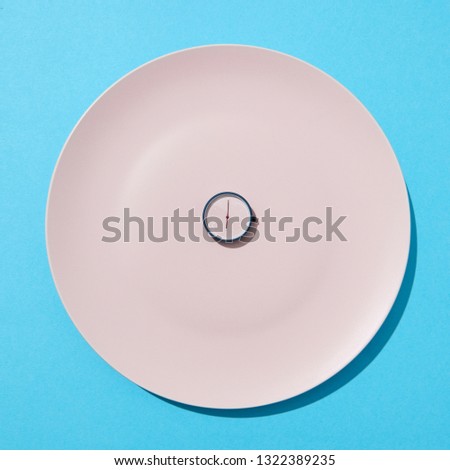 White plate with whatch shows six o'clock on a blue background, copy space. Flat lay. Concept of limiting the intake of food diet and weight loss.