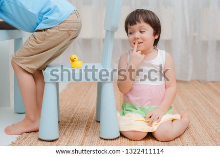 Sister puts a rubber duck on a chair under her brother's ass and hides on fool's day. Children's humor on April 1. Jokes and fun. Kids 3 years and 6 years Royalty-Free Stock Photo #1322411114