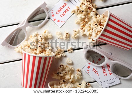 Overturned paper cups of tasty popcorn, cinema tickets and glasses on wooden background