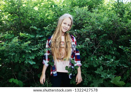 blonde teen girl wearing a plaid shirt posing in a green park, positive schoolgirl
