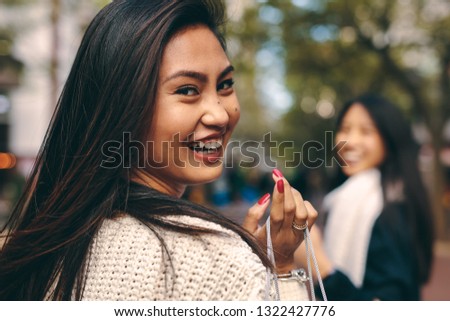 Portrait of a smiling woman holding a bag walking outdoors. Cheerful woman out for shopping with a friend looking back.