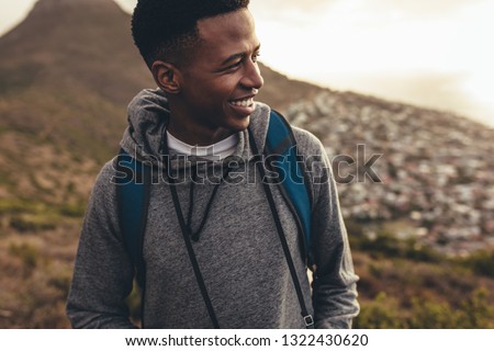 Smiling african man looking at the view while hiking. Social media influencer on hiking with his camera.