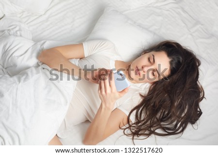 Young woman holding and using smart phone in the bed with feeling relax. Beautiful girl in bed. Close up image.