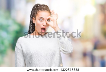 Young braided hair african american girl wearing winter sweater over isolated background doing ok gesture shocked with surprised face, eye looking through fingers. Unbelieving expression.