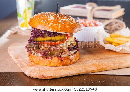 Juicy hamburger with beef burger cutlet, onion, lettuce, pickles, tomatos and cheese sauce in traditional buns, served on wood chopping board witn salad and French fries on served table. Copy space