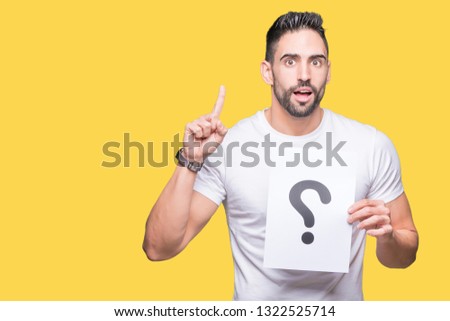 Handsome young man holding paper with question mark over isolated background surprised with an idea or question pointing finger with happy face, number one