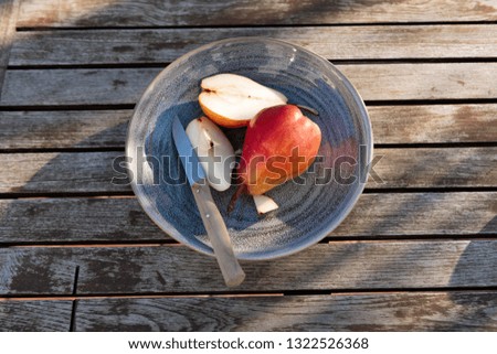 Red pears on blue plate cut in slices by knife in sunlight on wooden table.
