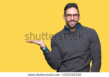 Young handsome man wearing glasses over isolated background smiling cheerful presenting and pointing with palm of hand looking at the camera.