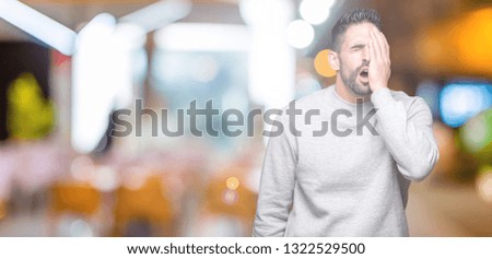 Young handsome man wearing sweatshirt over isolated background Yawning tired covering half face, eye and mouth with hand. Face hurts in pain.