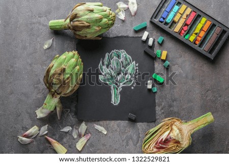 Tasty raw artichokes with picture on grey table