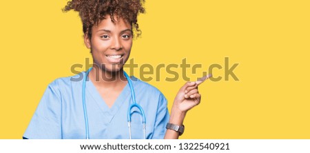 Young african american doctor woman over isolated background with a big smile on face, pointing with hand and finger to the side looking at the camera.
