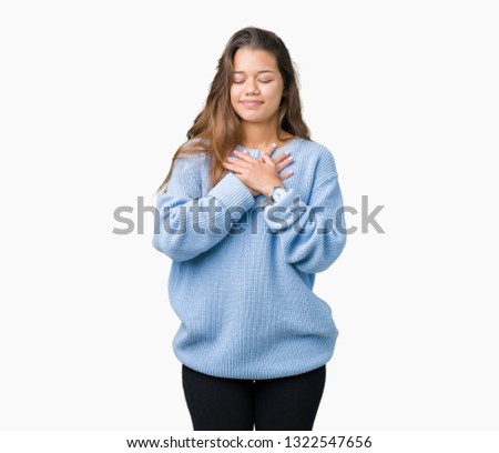 Young beautiful brunette woman wearing blue winter sweater over isolated background smiling with hands on chest with closed eyes and grateful gesture on face. Health concept.