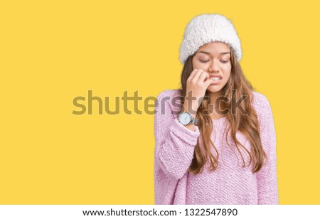 Young beautiful brunette woman wearing sweater and winter hat over isolated background looking stressed and nervous with hands on mouth biting nails. Anxiety problem.