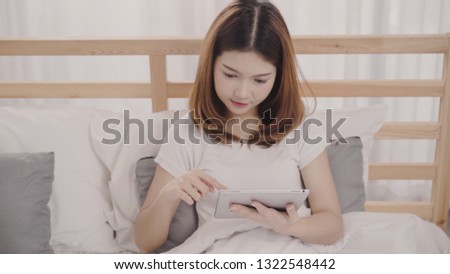 Young Asian woman using tablet while lying on bed after wake up in the morning, Beautiful attractive Japanese girl smiling relax in bedroom at home. Enjoying time lifestyle women at home concept.
