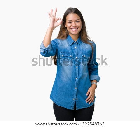 Young beautiful brunette woman wearing blue denim shirt over isolated background smiling positive doing ok sign with hand and fingers. Successful expression.
